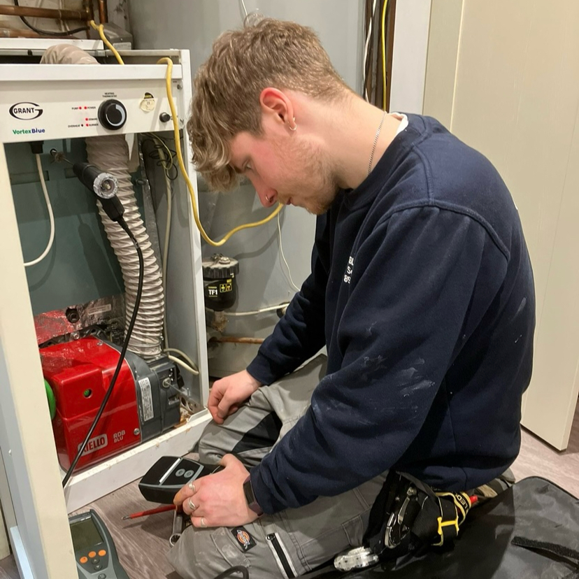 Zach servicing a Grant oil boiler, reading a flue gas analyser beside the red burner