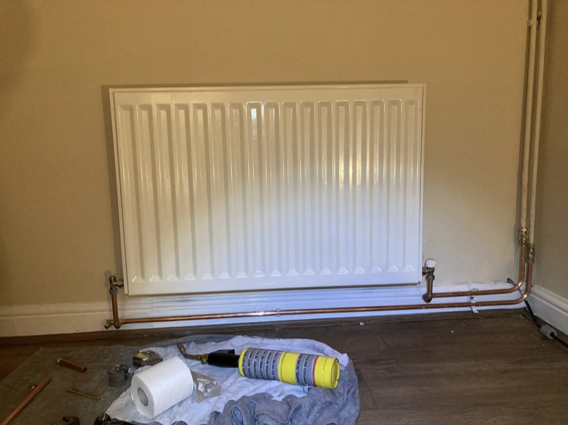 A newly fitted white radiator with copper pipework, dust sheets still down