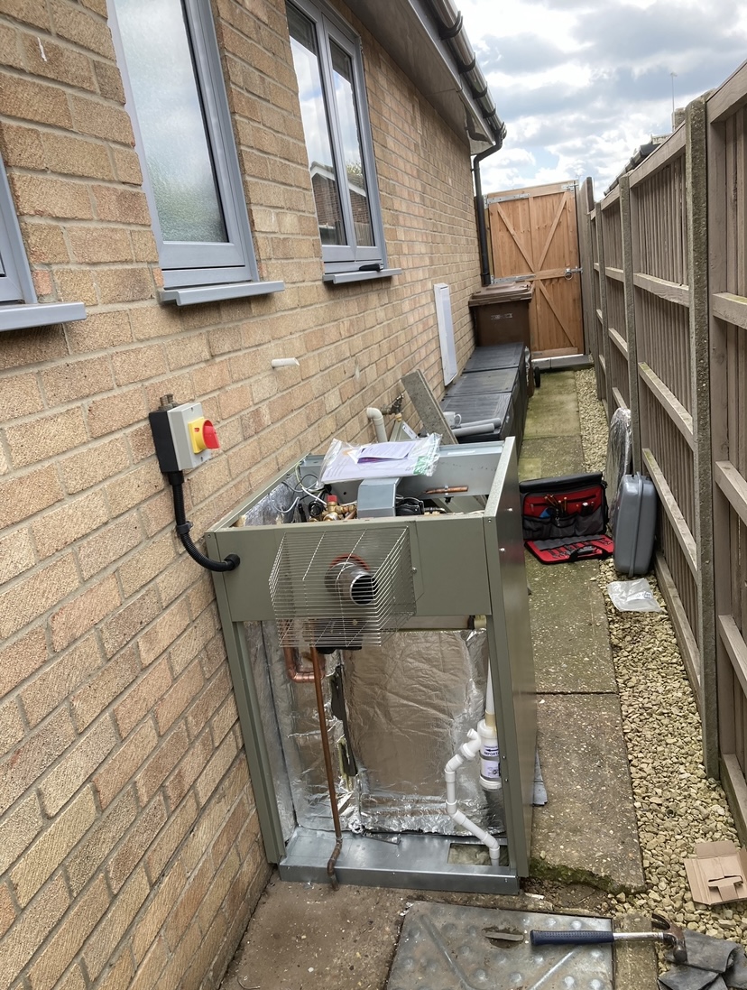 An outdoor oil boiler housing beside a bungalow wall with its isolator switch